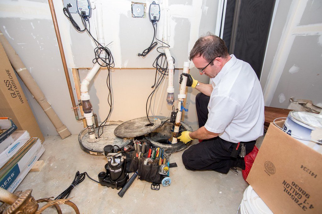 Technician installing new sump pump system in a residential basement with tools and wiring exposed